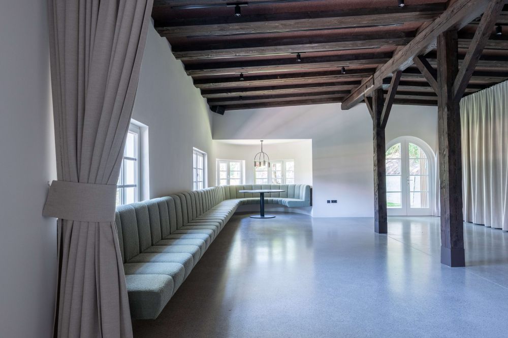 Innenansicht Eventraum mit salbeigrüner Sitzbank und historischen Holzbalken an der Decke und als Stützsäulen – ARKFORM